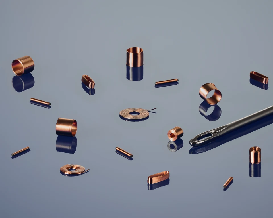 Small copper coils beside the eye of a sewing needle